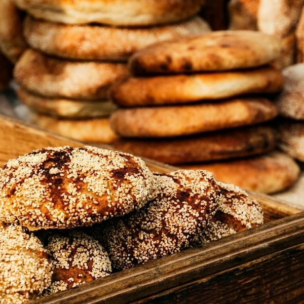 Freshly baked flatbreads, some topped with sesame seeds, displayed in wooden crates.