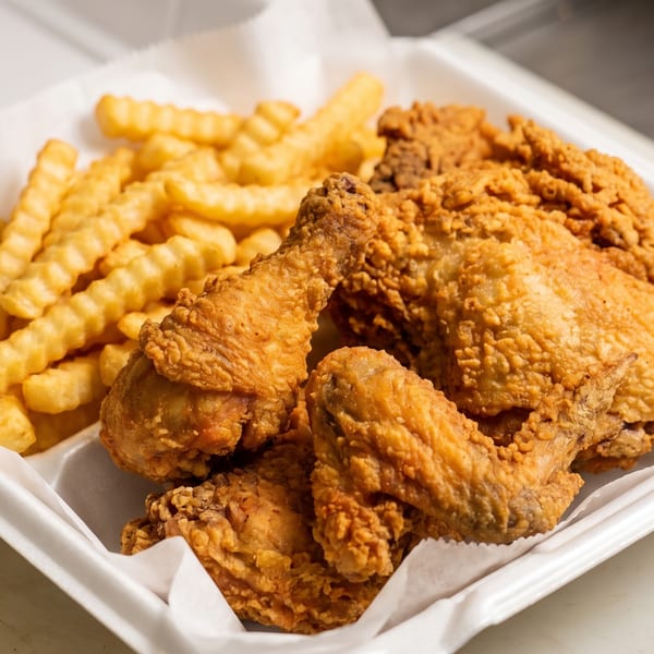 Crispy fried chicken pieces and crinkle-cut fries in a white takeout container.
